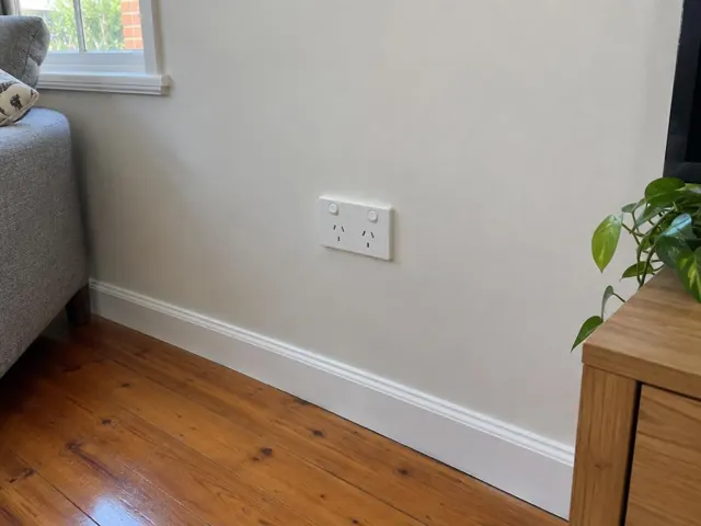 Dual power point on a painted living room wall above timber floorboards in Helensvale
