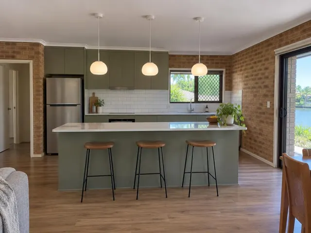 Kitchen with three pendant lights above island, olive cabinetry and brick walls in Hope Island